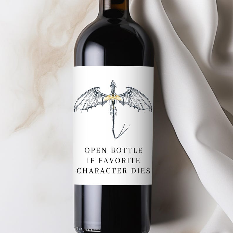 May include: A dark wine bottle with a white label featuring a dragon illustration with gold accents. The text on the label reads "OPEN BOTTLE IF FAVORITE CHARACTER DIES".