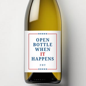 May include: A wine bottle with a white label featuring the text "OPEN BOTTLE WHEN IT HAPPENS" in blue and red. The label is framed with a red border and stars. The bottle is filled with a light yellow liquid.