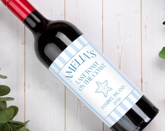 May include: A wine bottle with a red screw cap and a custom label featuring light blue and white vertical stripes. The label text reads AMELIA'S LAST TOAST ON THE COAST, SANIBEL ISLAND 2026, accompanied by a blue starfish graphic illustration.