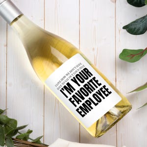May include: A clear glass wine bottle filled with white wine, featuring a white rectangular label with black text that reads: I LOVE HOW WE DON'T HAVE TO SAY OUT LOUD THAT I'M YOUR FAVORITE EMPLOYEE. The bottle has a silver metallic cap.