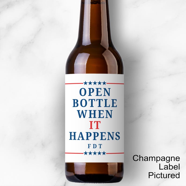 May include: A brown glass bottle with a white label. The label reads "OPEN BOTTLE WHEN IT HAPPENS" in blue and red text, with stars and lines. The bottle is on a white marble surface.
