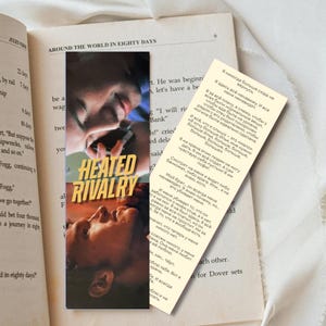 May include: A bookmark with the title "Heated Rivalry" and images of two people. The bookmark is placed in an open book titled "Around the World in Eighty Days". A handwritten note in Russian is next to the bookmark.