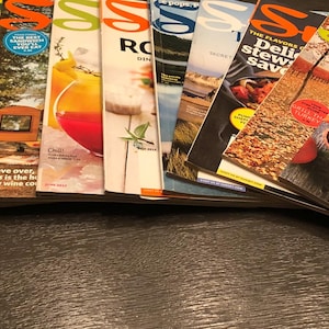 Peut inclure: Une pile de magazines Sunset présentant divers sujets culinaires et de style de vie, notamment des recettes de dîners sains, de ragoûts délicieux et d'idées de cadeaux de fêtes.