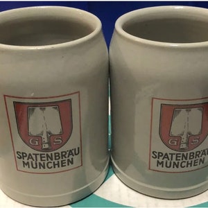 May include: Two white ceramic beer steins with a red and white logo that says "Spatenbräu München" and a graphic of a shovel.