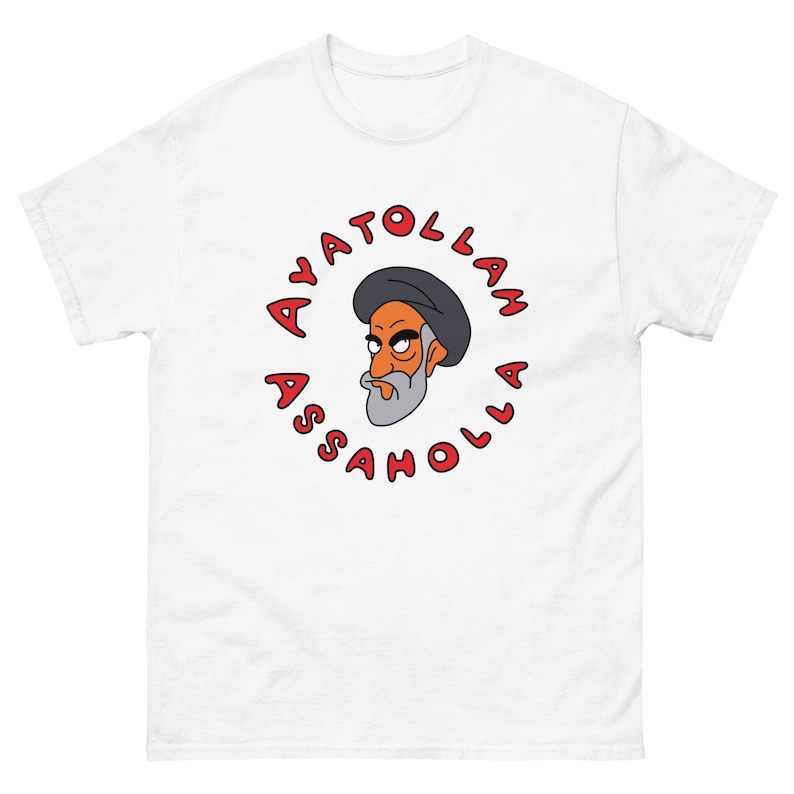 May include: A white t-shirt with a red circle graphic. The graphic features a cartoon image of a man with a beard and a black turban. The text around the image reads 'Ayatollah Assahola'.