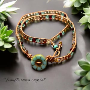 Könnte beinhalten: Ein doppeltes Wickelarmband aus Kristall mit einem türkisfarbenen Knopfverschluss. Das Armband besteht aus braunem Lederband und mehrfarbigen Glasperlen.