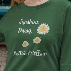 May include: A green long-sleeved shirt with the text "Sunshine Daisy Butter Mellow" and three white daisies with yellow centers.