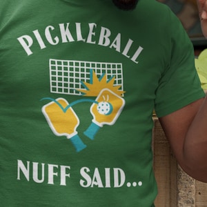 May include: Green t-shirt with a white graphic of two pickleball paddles hitting a ball over a net. The text "Pickleball Nuff Said..." is printed below the graphic.
