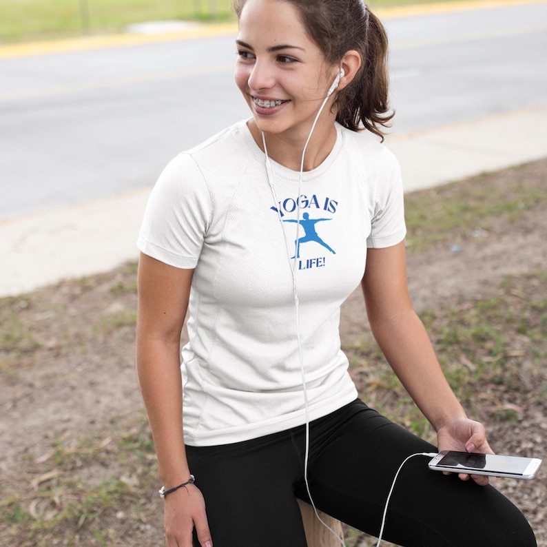 Puede incluir: Una camiseta blanca con un gr&aacute;fico azul que dice "Yoga is Life!" y una silueta azul de una persona haciendo yoga.