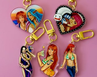 May include: Collection of acrylic keychains featuring anime characters. The keychains have gold-colored clasps and depict various female characters in vibrant colors. One keychain is heart-shaped, while others are rectangular.