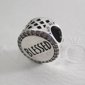 Puede incluir: Encanto de plata con un borde de cristal transparente y la palabra "Blessed" en letras negras. El encanto tiene un patr&oacute;n de celos&iacute;a decorativo en la parte posterior y la inscripci&oacute;n "S 925 ALE" en el lateral.