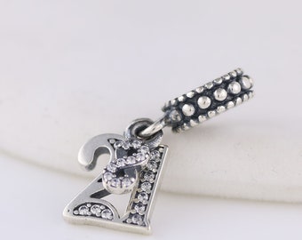 May include: Silver charm with the number 21 decorated with clear cubic zirconia stones. The charm has a small loop at the top for attaching to a bracelet or necklace.