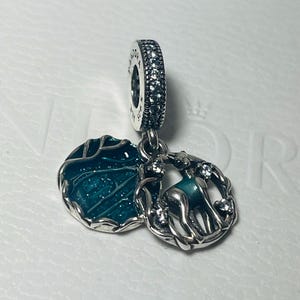 May include: A silver charm with a green enamel circle and a silver deer with a green enamel body and clear crystal accents. The charm is designed to be added to a bracelet or necklace.