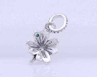 May include: A silver charm in the shape of a four-leaf clover with a green gemstone in the center. The charm has a loop at the top for attaching to a bracelet or necklace.