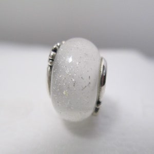 May include: A white glass bead with silver glitter and a silver metal accent.