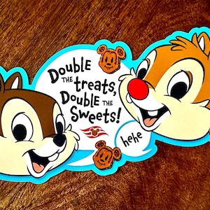 May include: A blue and white speech bubble with the text "Double the treats, Double the Sweets!" and a cartoon image of Chip and Dale. Chip and Dale are smiling and have red noses. The speech bubble has a red and white ship's wheel logo.