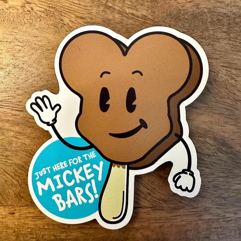 May include: A brown cartoon ice cream bar with a smiling face and stick, waving with a white gloved hand. The ice cream bar is on a blue circle with the text "Just here for the Mickey Bars!"