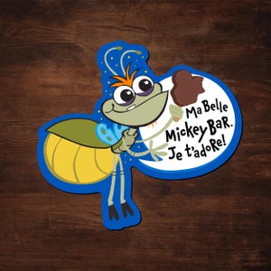 May include: A die-cut sticker featuring a cartoon firefly holding a Mickey Bar ice cream. The firefly is green and yellow with orange hair and large eyes. Text on the sticker reads "Ma Belle Mickey Bar. Je t'adore!"