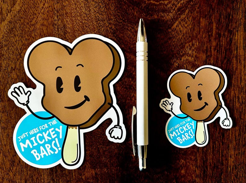 May include: Two brown and white cartoon ice cream bars with a smiling face and arms. The larger ice cream bar has a blue circle with the text "Just here for the Mickey Bars!" The smaller ice cream bar has a blue circle with the text "Just here for the Mickey Bars!"