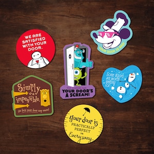 Op de afbeelding: Een verzameling kleurrijke stickers met verschillende ontwerpen en tekst. Eén sticker toont Baymax, een andere Mickey Mouse met zonnebril, en andere tonen zinnen als "Your Door's a Scream!" en "Simply Impossible".