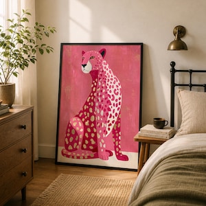 May include: A framed art print featuring a stylized cheetah in shades of pink, white, and gold. The cheetah is depicted in a seated pose against a pink background. The artwork is framed in a black border and adds a touch of modern decor.