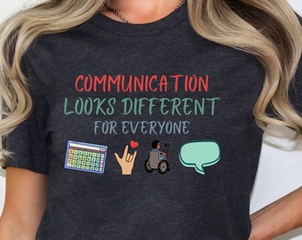 Puede incluir: Camiseta de color gris oscuro jaspeado con el texto "COMMUNICATION LOOKS DIFFERENT FOR EVERYONE" y tres iconos: un teclado, una mano haciendo el signo de la lengua de señas americana para "Te amo" y una persona en silla de ruedas usando una computadora.
