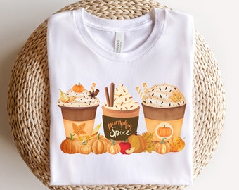 May include: White t-shirt with a graphic of three pumpkin spice lattes with whipped cream and sprinkles. The lattes are surrounded by fall leaves and pumpkins. The text "Pumpkin Spice" is written on the middle latte.