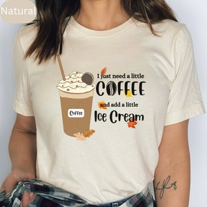 May include: A cream-colored t-shirt featuring a graphic of a coffee drink with whipped cream and a cookie. The text reads "I just need a little COFFEE and add a little Ice Cream". Autumn leaves are also included in the design.