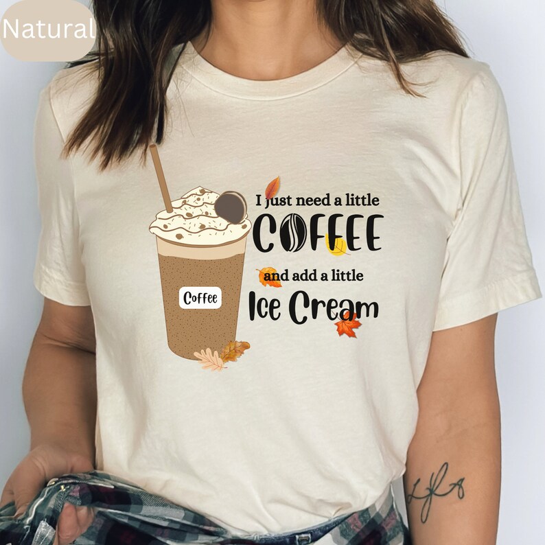 May include: A cream-colored t-shirt featuring a graphic of a coffee drink with whipped cream and a cookie. The text reads "I just need a little COFFEE and add a little Ice Cream". Autumn leaves are also included in the design.