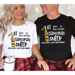 May include: A couple wearing matching Christmas themed t-shirts with a beer bottle graphic and the text "ST JINGLE NO BELLS COCKTAILS CHRISTMAS SOBER STILL JOLLY, JUST LESS WOBBLY".