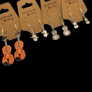 May include: Four pairs of silver violin dangle earrings on brown card stock with the text "Handmade with love".