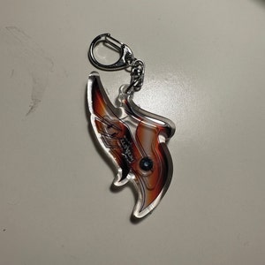 May include: A red and orange acrylic keychain with a silver metal ring. The keychain features a stylized image of a wing with the word "MILLENNIUM" printed on it.