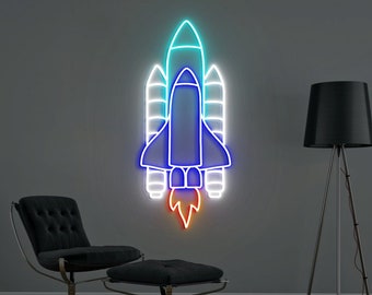 Könnte beinhalten: Ein Neon-Schild, das ein blaues und weißes Raumschiff mit orangefarbenen Flammen zeigt, vor einer grauen Wand. Das Schild leuchtet und hängt an der Wand.
