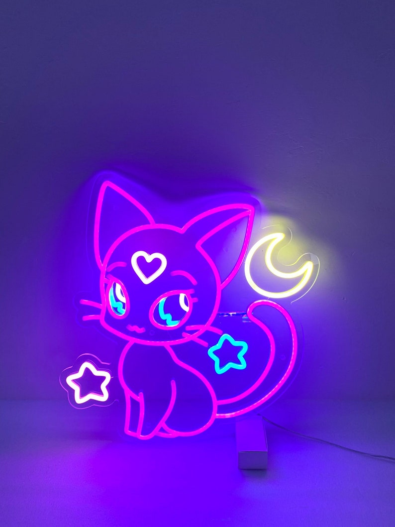 May include: A neon sign shaped like a cartoon cat with a crescent moon behind it. The cat is pink and has blue eyes and a heart on its chest. The moon is yellow and there are two stars in the background.
