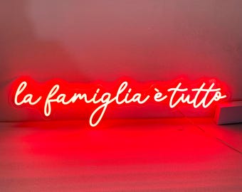 Può includere: Un cartello al neon bianco con la frase italiana "la famiglia è tutto", che significa "la famiglia è tutto", su uno sfondo rosso.