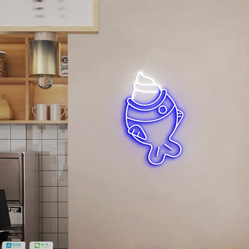 May include: A neon sign in the shape of a fish with a scoop of ice cream on top. The sign has a blue outline with a white ice cream scoop. The sign is mounted on a light beige wall.