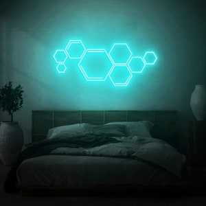 Puede incluir: Un dormitorio con una luz de neón azul verdoso en forma de panal en la pared. La cama tiene una cabecera gris oscuro y un edredón gris oscuro.