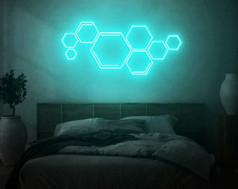 May include: A bedroom with a teal blue neon light shaped like a honeycomb on the wall. The bed has a dark gray headboard and a dark gray comforter.