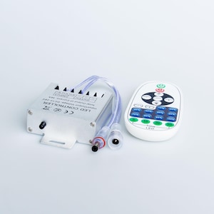 Może przedstawiać: Kontroler LED ze srebrną metalową obudową i białym pilotem. Kontroler posiada porty wejściowe i wyjściowe, a pilot przyciski do ustawiania trybu, prędkości i czasu. Widoczny jest napis "LED CONTROLLER".