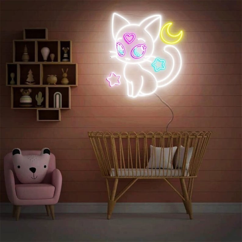 May include: A white neon sign of a cat with a crescent moon and stars. The cat has pink and blue eyes and a pink heart on its forehead. The sign is lit up and is hanging on a wall.