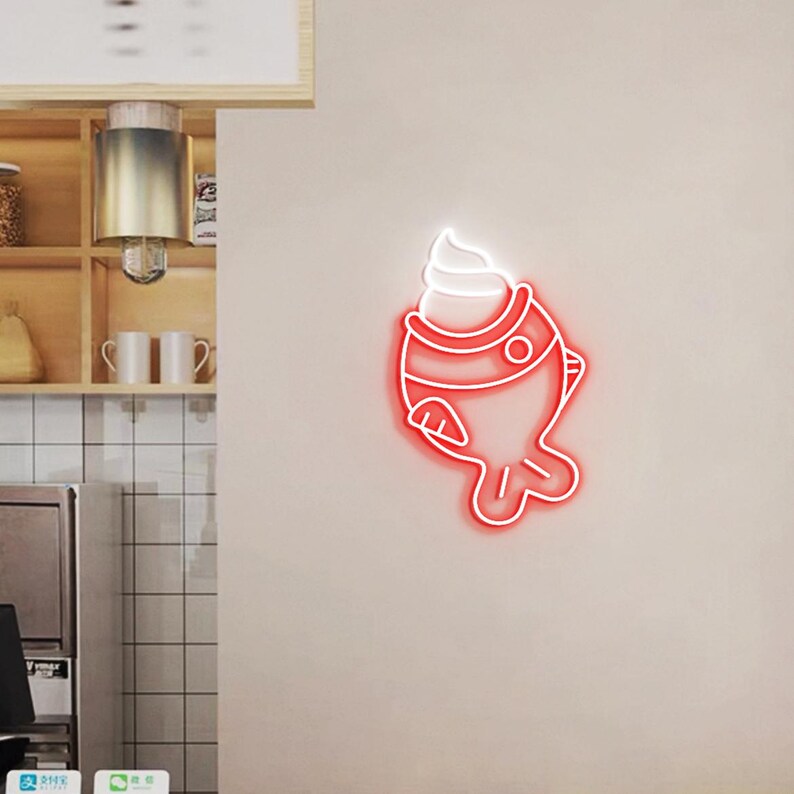May include: A red neon sign shaped like a fish with a swirl of white ice cream on top. The sign is mounted on a light beige wall. The sign is a decorative element.