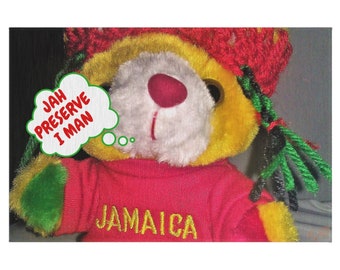Pode incluir: Um urso de pelúcia amarelo vestindo um chapéu vermelho e verde e uma camisa vermelha com a palavra "JAMAICA" bordada. O urso está pensando em uma bolha de pensamento que diz "JAH PRESERVE I MAN".