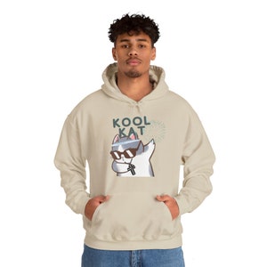 May include: A beige hoodie with a graphic of a cat wearing sunglasses and a party hat. The text "KOOL KAT" is above the cat graphic.