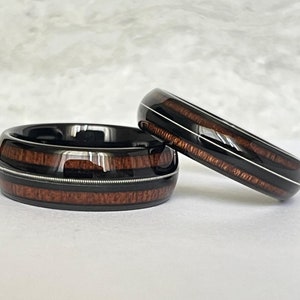 Könnte beinhalten: Zwei schwarze und braune Holz-Inlay-Eheringe mit silbernen Akzenten. Die Ringe sind übereinander gestapelt.