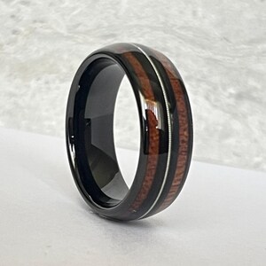 May include: A black tungsten carbide ring with a brown wood inlay and a silver stripe.