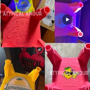 May include: A collection of four small, square, four-legged plastic stands in bright pink and yellow. The stands feature embossed text including The Glow Bar, Easy Peasy Squeezy Lemonade, and Lemenager's Lemonade, along with a cartoon lemon graphic.