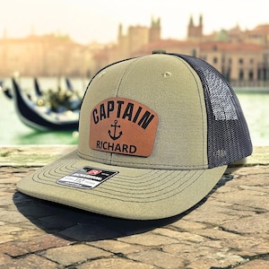 May include: A green and black trucker hat with a brown leather patch that says "Captain Richard" with an anchor symbol.