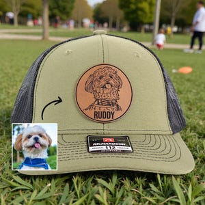 May include: Olive green Richardson 112 trucker hat with a black mesh back. A circular leather patch features a dog portrait and the name "Ruddy". The hat has an adjustable strap.
