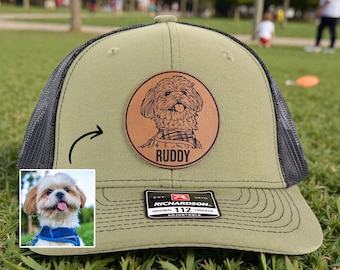 May include: Olive green Richardson 112 trucker hat with a black mesh back. A circular leather patch features a dog portrait and the name "Ruddy". The hat has an adjustable strap.