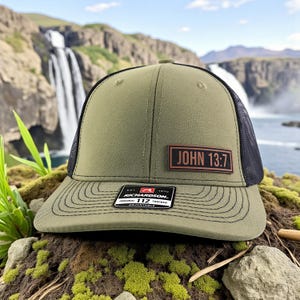 May include: Olive green trucker hat with a black mesh back and a curved brim. The hat features a rectangular patch with the text "JOHN 13:7". A small tag on the brim reads "RICHARDSON ORIGINAL 112 TRUCKER".